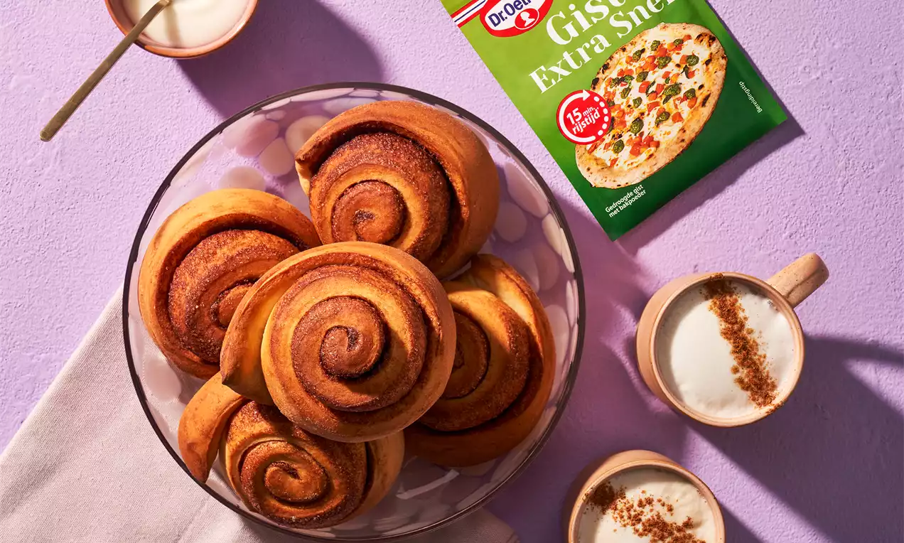 Goudbruine cinnamonrolls met een glanzende, gekarameliseerde bovenkant in een glazen schaal op een zachte paarse ondergrond