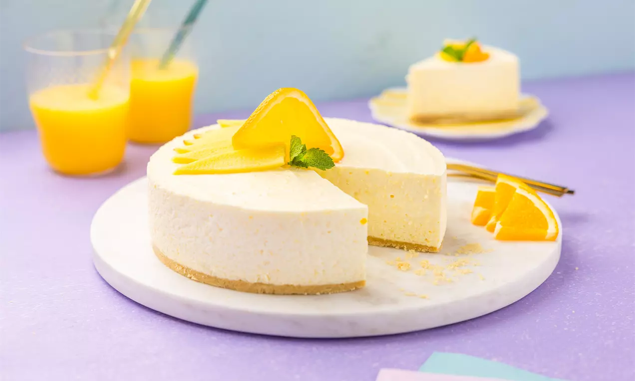 Ronde sinaasappel-mango kwarktaart met romige vulling op een zandkleurige bodem, gegarneerd met sinaasappelschijfjes en munt op een wit bord