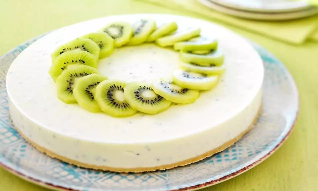 Ronde kiwi kwarktaart met gladde witte vulling en zachtbruine bodem, gegarneerd met een ring van groene kiwiplakjes op een patroonbord