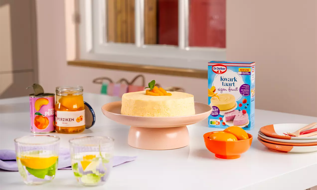 Perzik kwarktaart met gladde, lichtgele vulling en een glanzende perziktopping, geserveerd op een roze taartplateau met muntblaadje