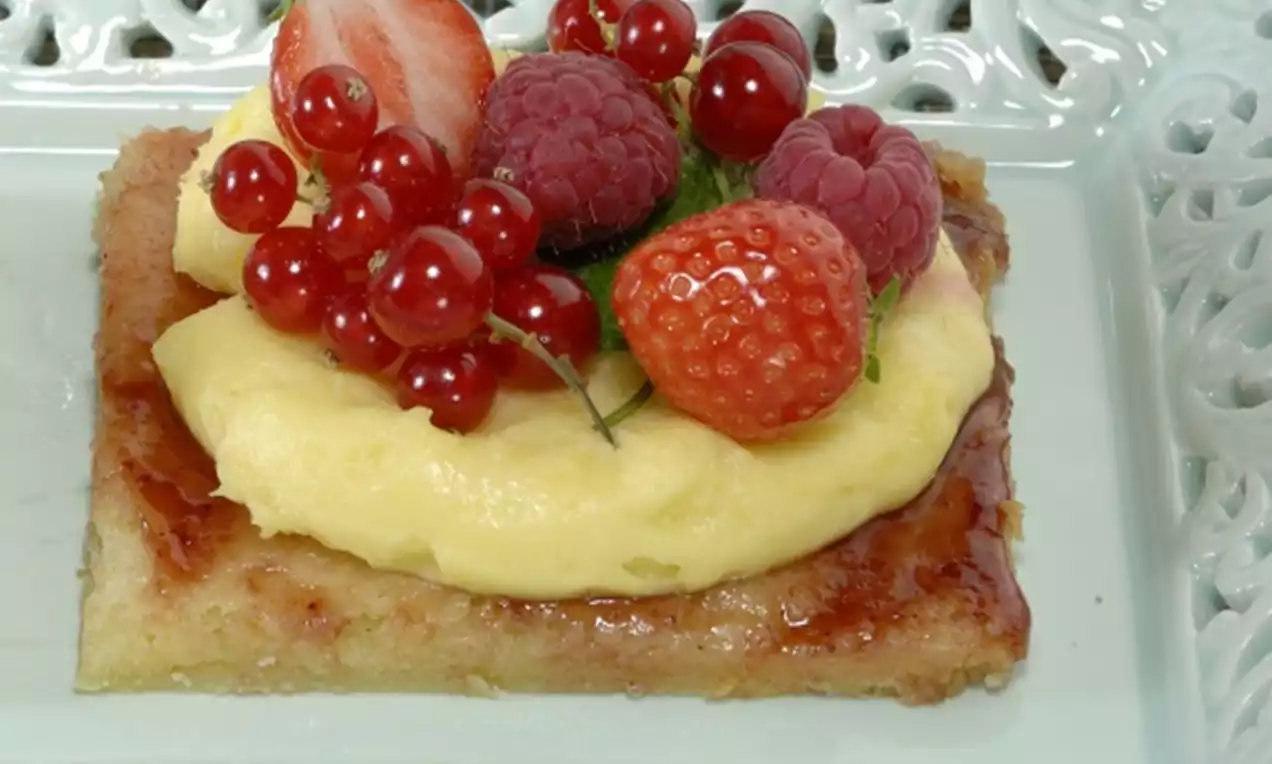 Kruimelkoek met een laagje glanzende banketbakkersroom, gedecoreerd met rode bessen, frambozen en aardbeien op een pastelgroen bord