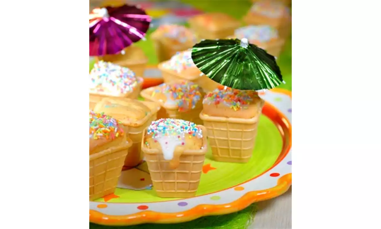 IJsvormige cakejes met beige wafelbodems, witte glazuur en kleurrijke sprinkles, geserveerd op een kleurrijk bord met papieren parasols